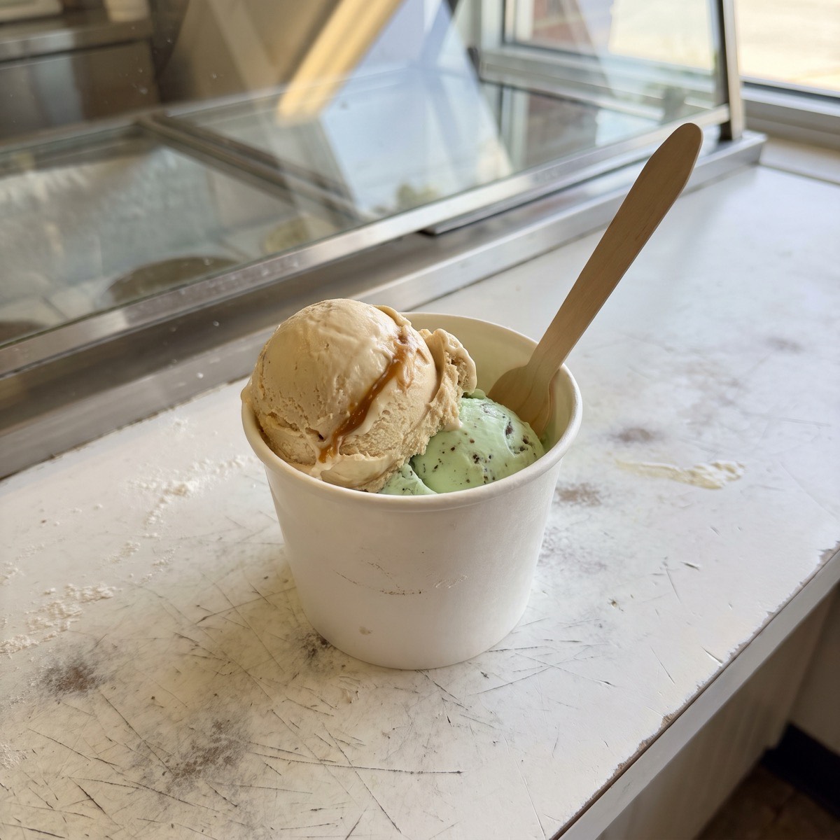 A cup with scoops of salted caramel and mint chip ice cream and a wooden spoon